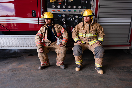 A pair of firefighters sit on the edge of a firetruck.